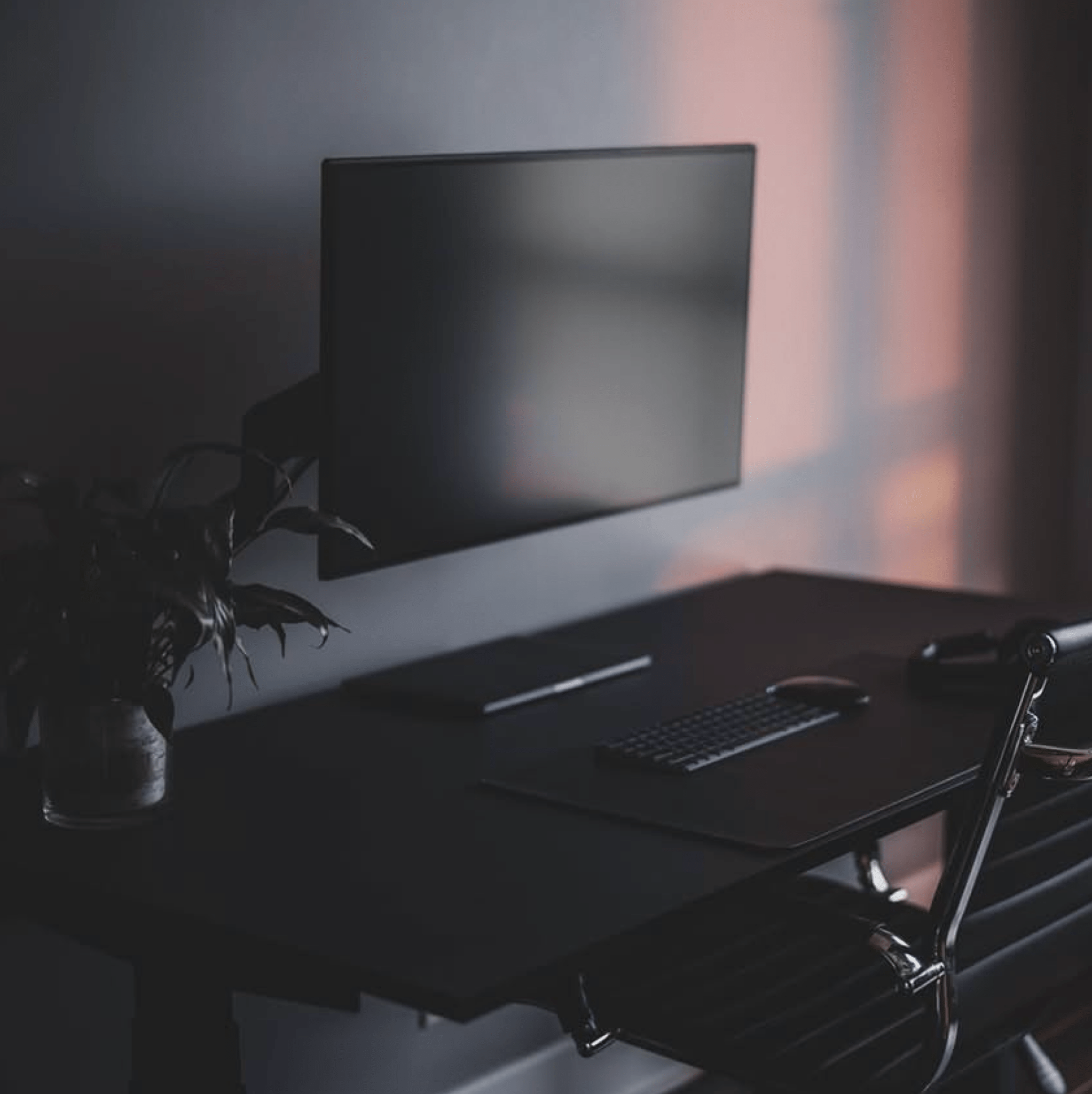 Modern office desk setup with a computer monitor, keyboard, and mouse in a dimly lit room.